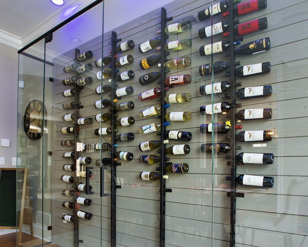 Wine bottles displayed on a wall rack inside a glass-enclosed area, lit with purple lights.