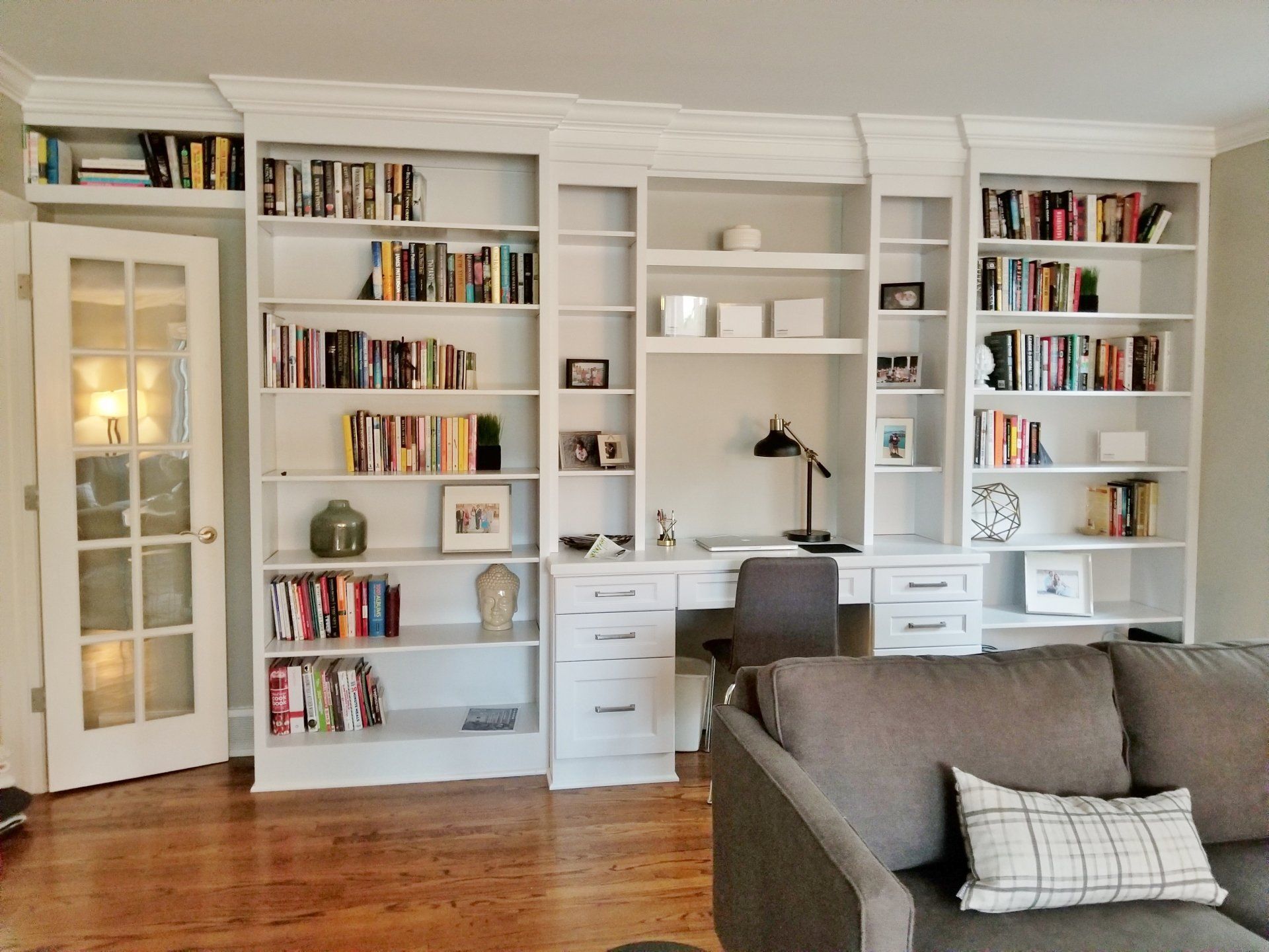 White built-in bookshelves with a desk and a sofa in front of a wooden floor.