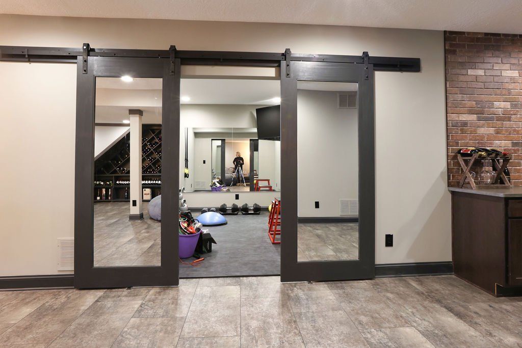 Two dark framed sliding mirrored doors open to a home gym with exercise equipment.