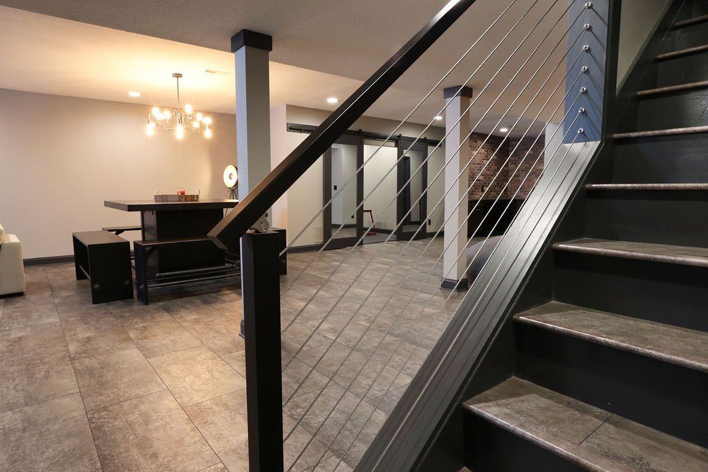 Basement with stairs and cable railing. Dark stairs, wood flooring, and living area in the background.