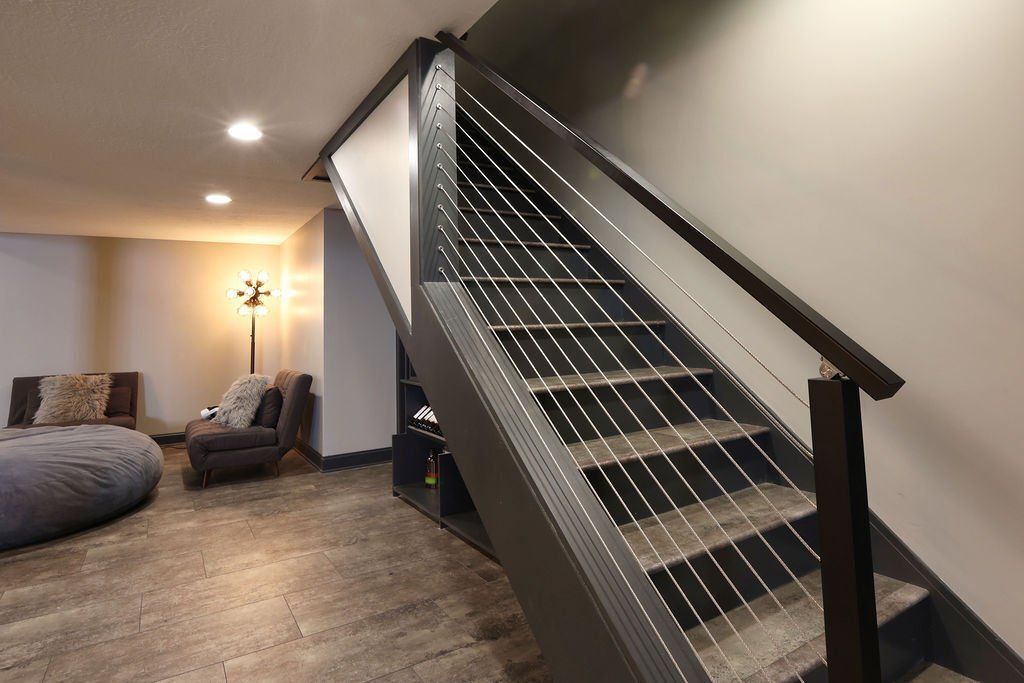 Staircase with metal cable railings leading to a living space. Gray and brown tones.