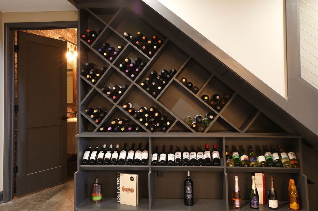 Wine rack built into a staircase with gray shelves holding many bottles of wine. Doorway visible.