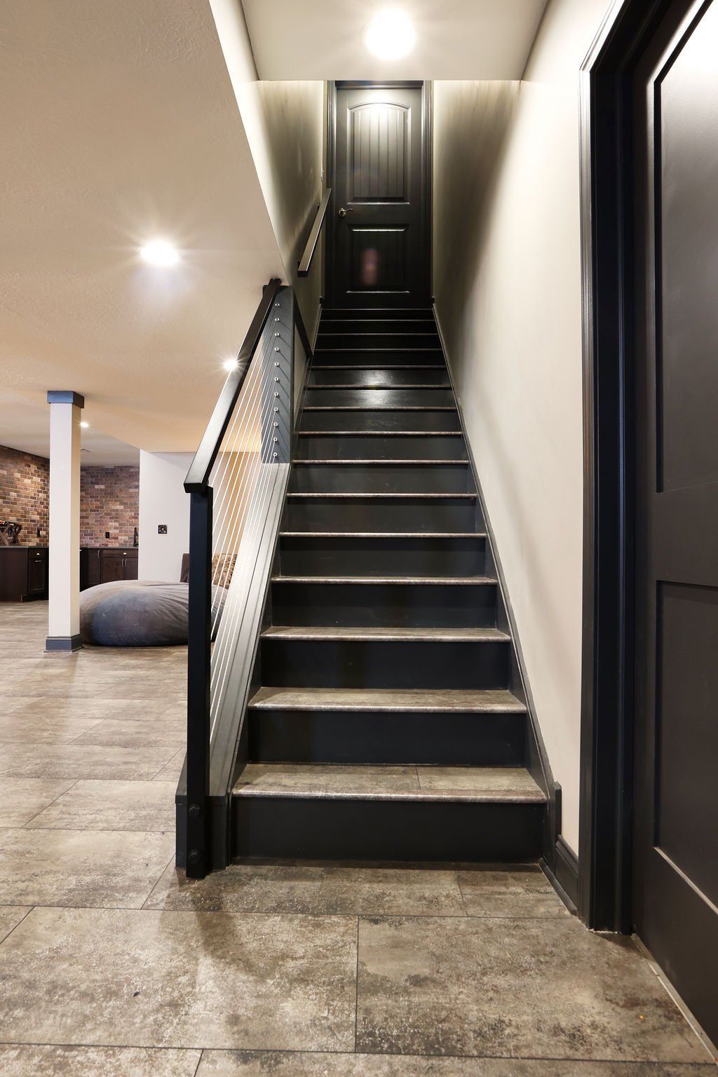 Staircase leading up to a closed black door. Black stairs, black railing, tan walls.