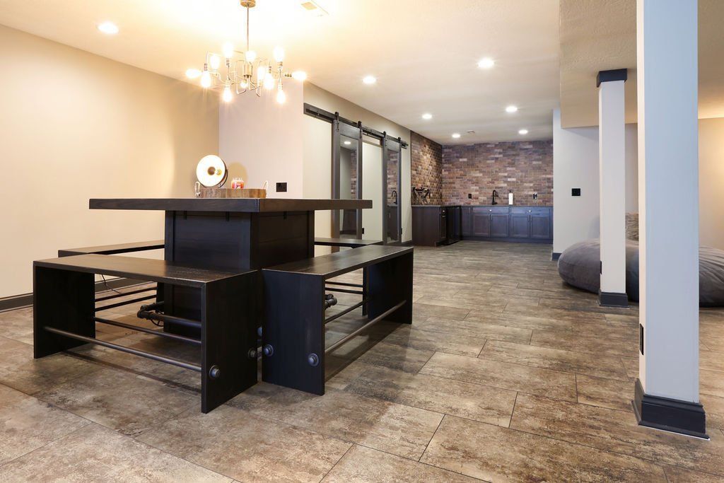 Spacious basement with a dark table and benches, stone accent wall, and a modern chandelier.