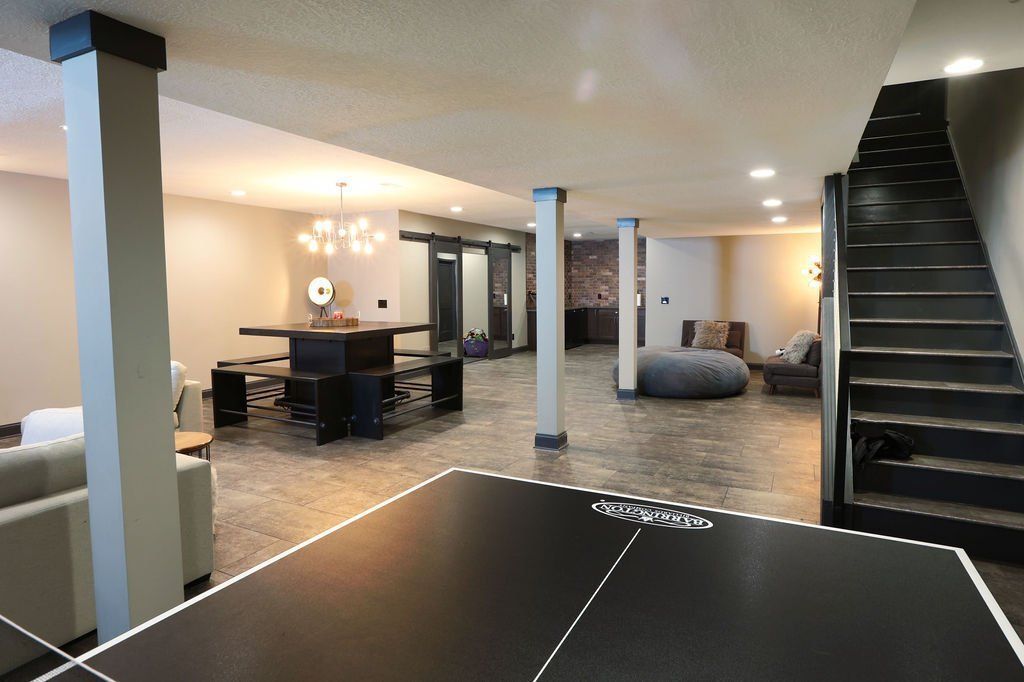 Basement with ping pong table, dining table, seating area, and stairs. Concrete floor, neutral colors, and exposed beams.