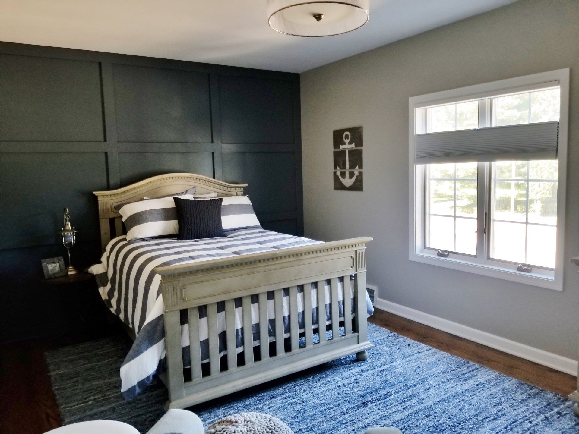Bedroom with navy accent wall, gray bed, blue rug, and nautical decor.