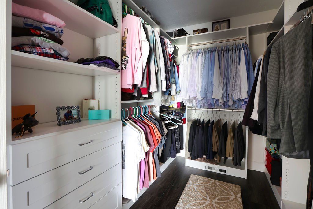 Walk-in closet with white shelves and drawers, clothes hanging on racks, and various items stored.