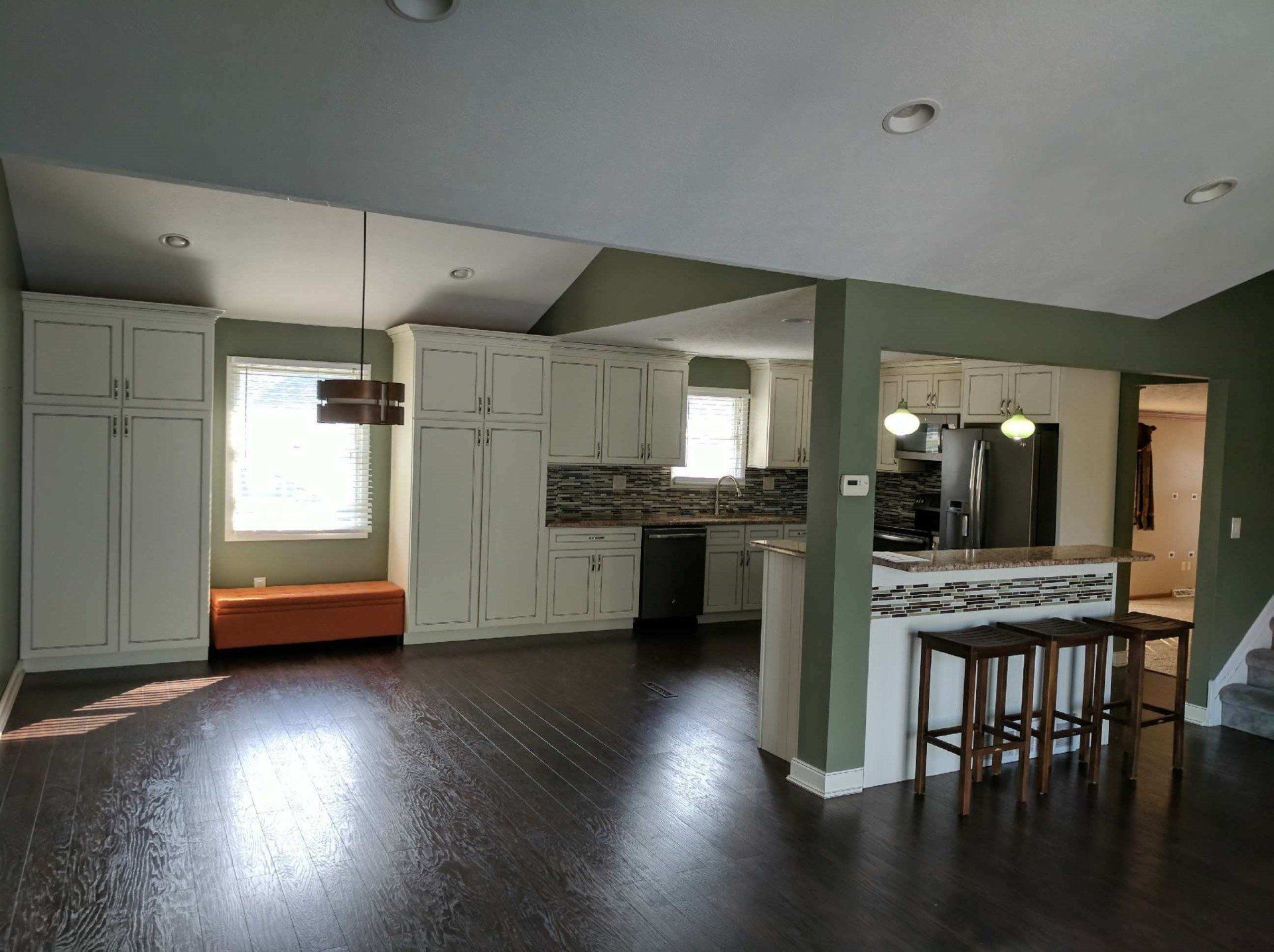 Open-concept kitchen with white cabinets, a dark floor, and a breakfast bar with stools.