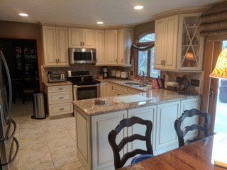 Cream-colored kitchen with granite countertops, a microwave, and a breakfast bar with two chairs.