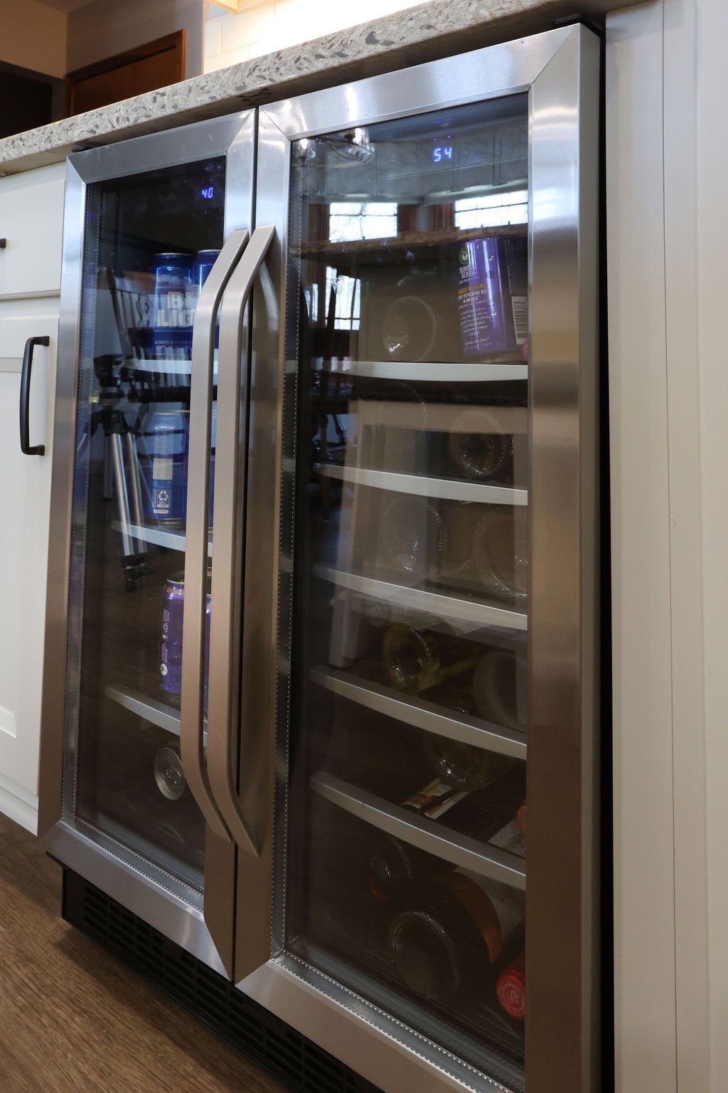 Stainless steel double-door beverage center built into a white cabinet, under a countertop.