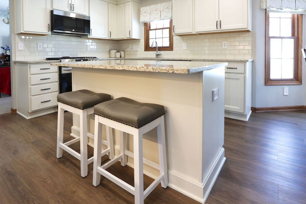White kitchen with island and two gray stools. Dark wood floor.