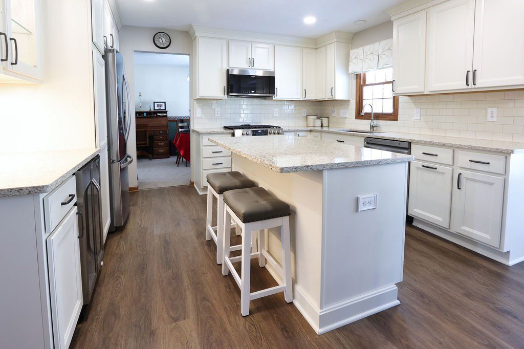 White kitchen with island, granite countertops, and dark wood flooring.