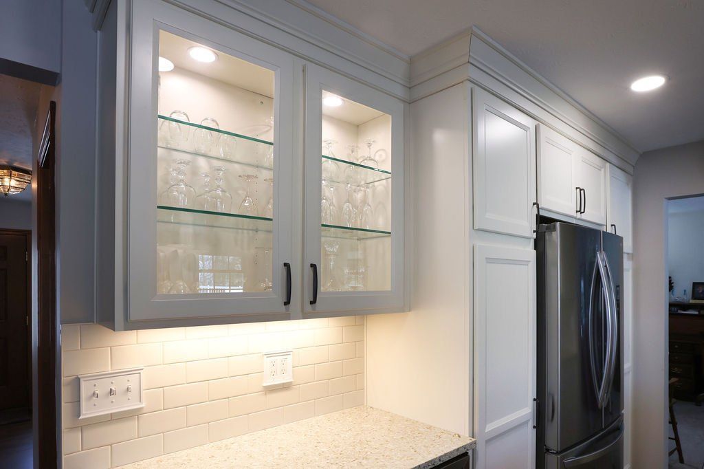 White kitchen cabinets with glass-front display, under-cabinet lighting, and stainless steel refrigerator.