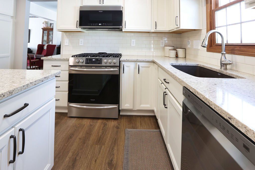 Bright kitchen with white cabinets, granite countertops, stainless steel appliances, and dark wood floors.