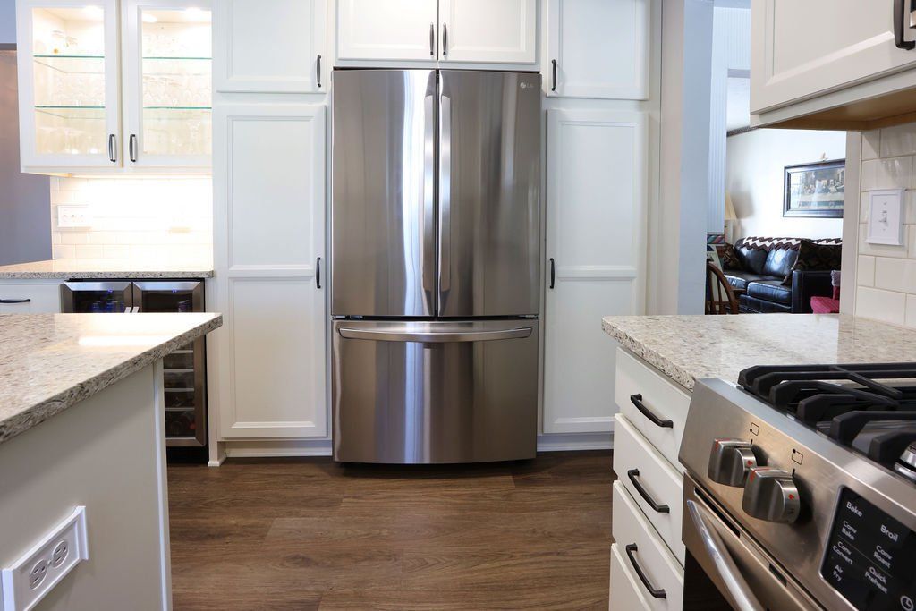 Modern kitchen with stainless steel refrigerator, white cabinets, granite countertops, and dark wood flooring.