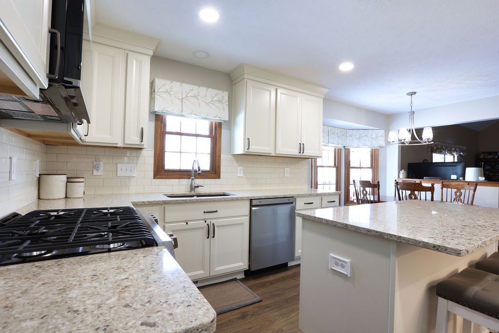 Bright kitchen with granite island, white cabinets, gas stove, and stainless steel dishwasher in a home.