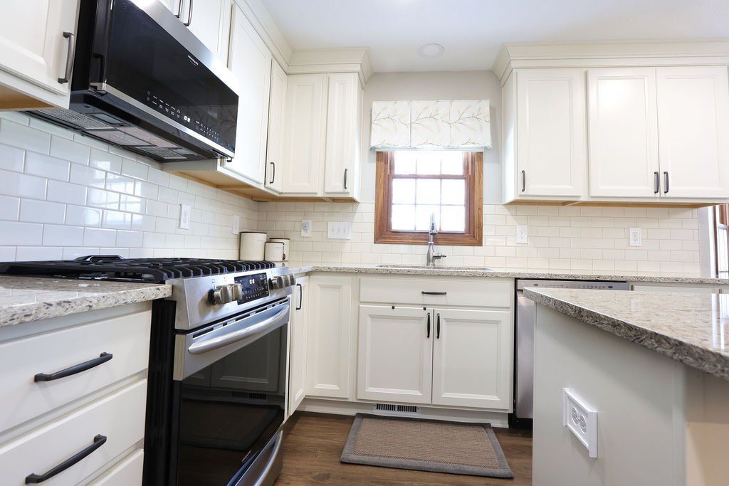 Bright white kitchen with granite countertops, black stove, and a window above the sink