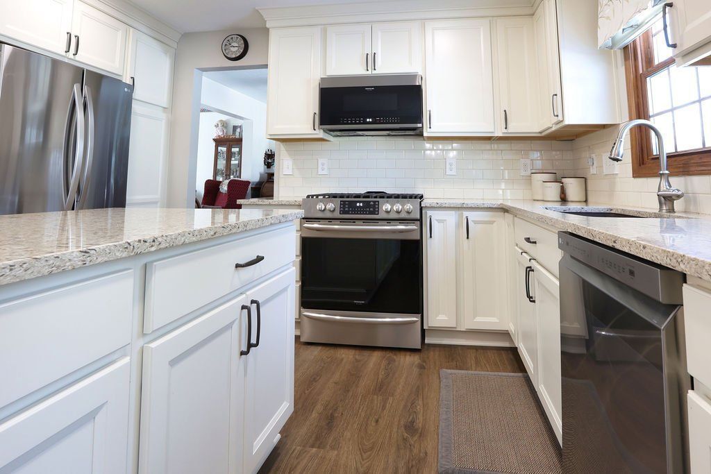 White kitchen with stainless steel appliances, granite countertops, and brown wood floors.