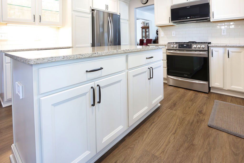 White kitchen with island and stainless steel appliances, light-colored cabinets, and wood-look flooring.