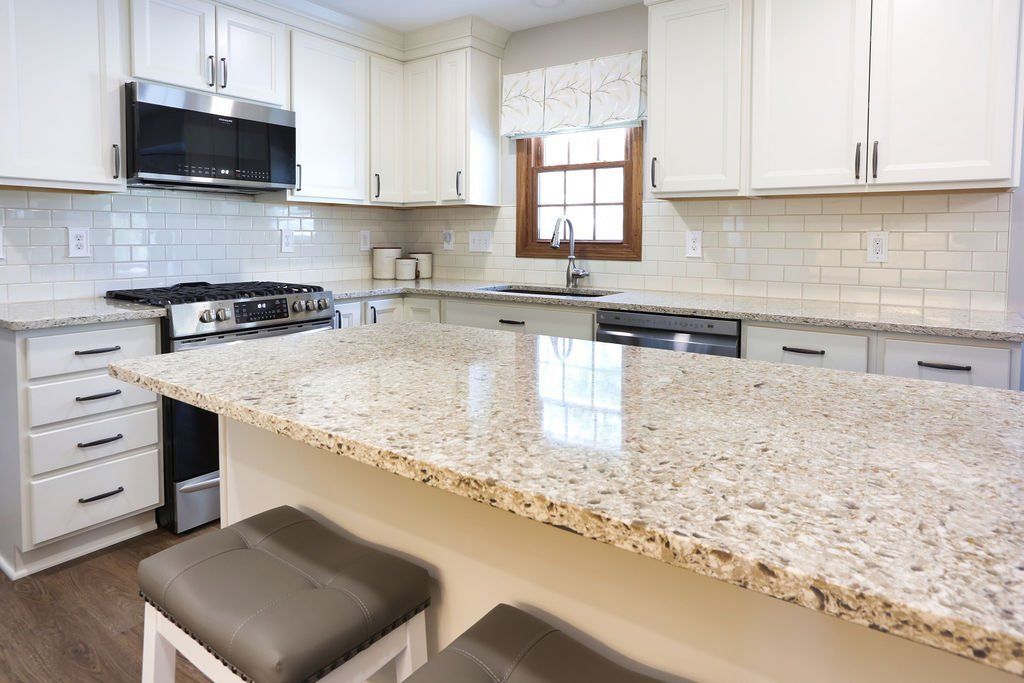 White kitchen with granite countertops, stainless steel appliances, and bar stools.
