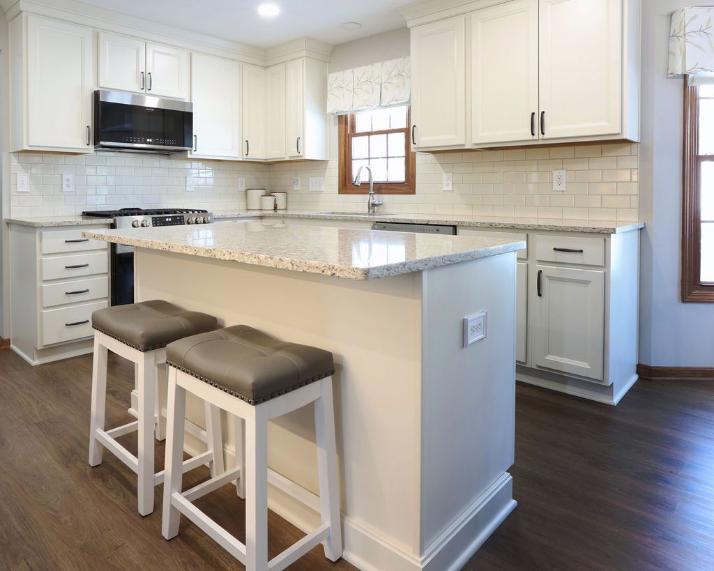 White kitchen with island, granite countertop, and two gray stools.