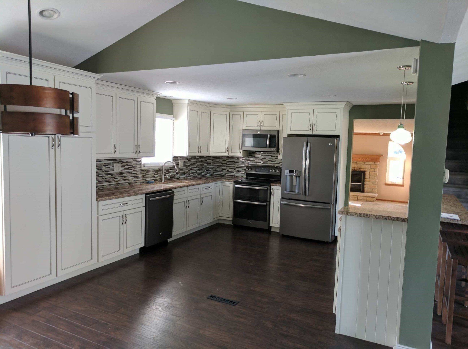 Bright kitchen with white cabinets, stainless appliances, dark wood floor, and green walls