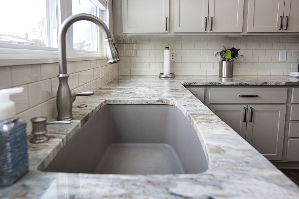 Modern kitchen sink with large faucet, marble countertop, and gray cabinets