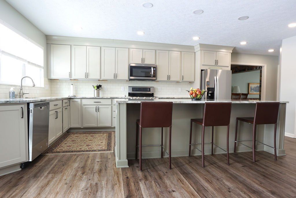 Modern kitchen with light cabinets, stainless steel appliances, and brown bar stools.