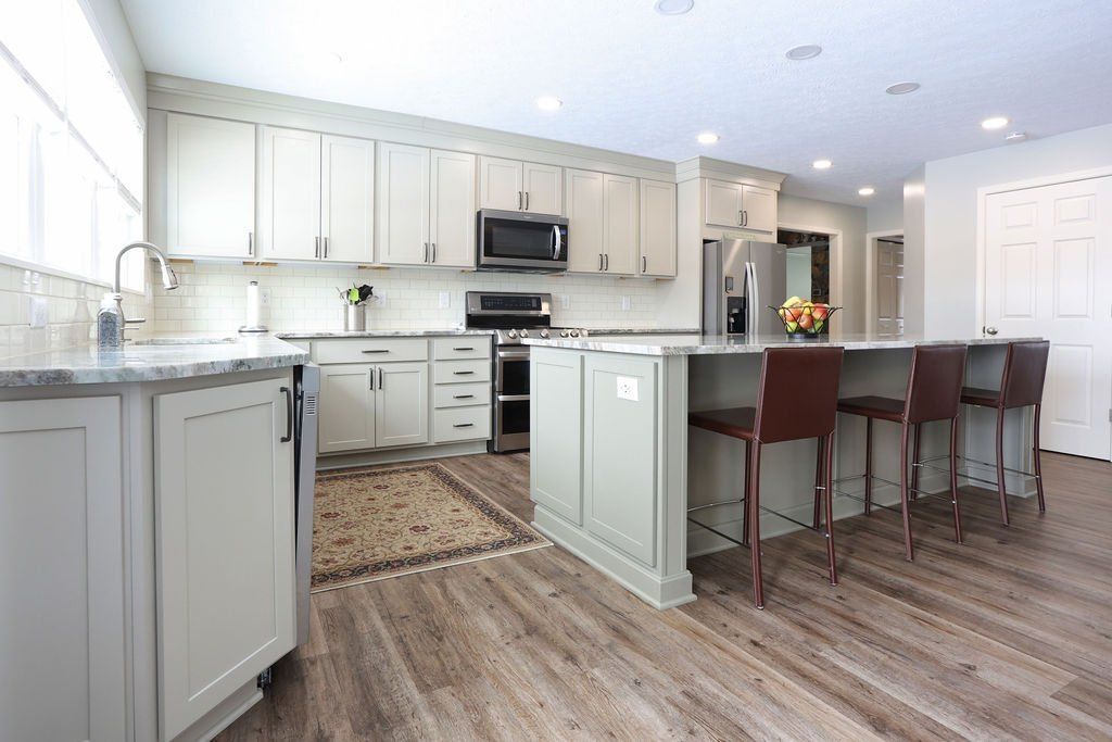 Bright white kitchen with gray cabinets, stainless appliances, and a large island with bar stools.