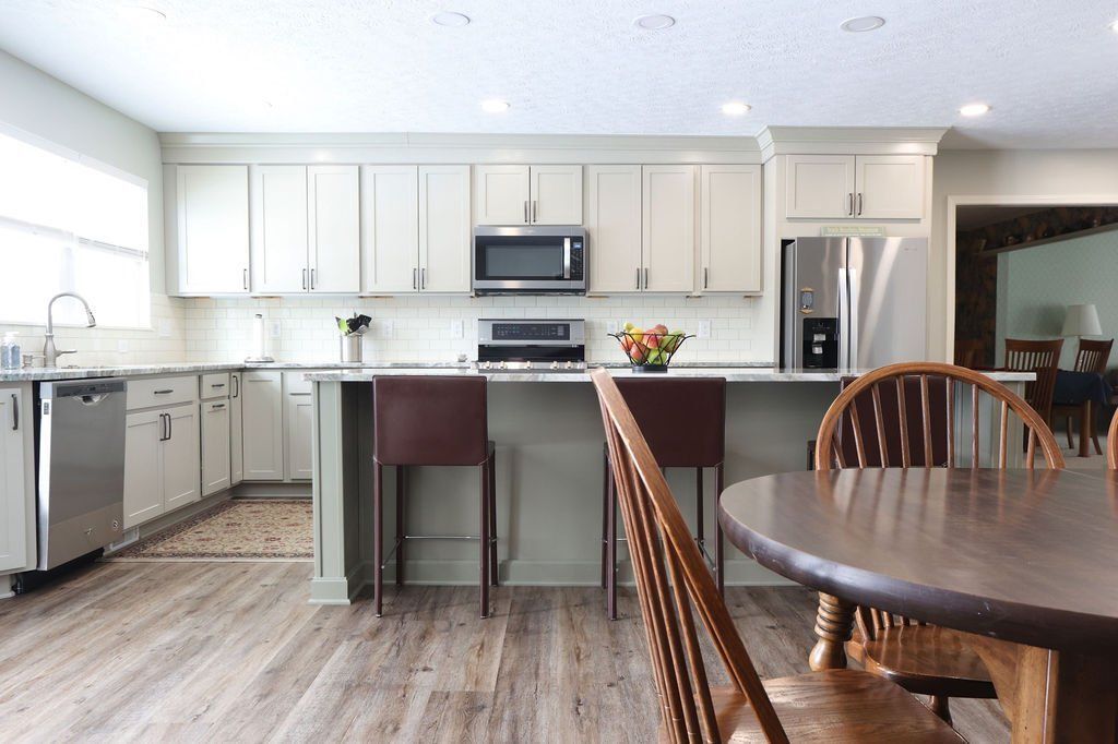 Kitchen with light green cabinets, stainless steel appliances, and wooden floor.