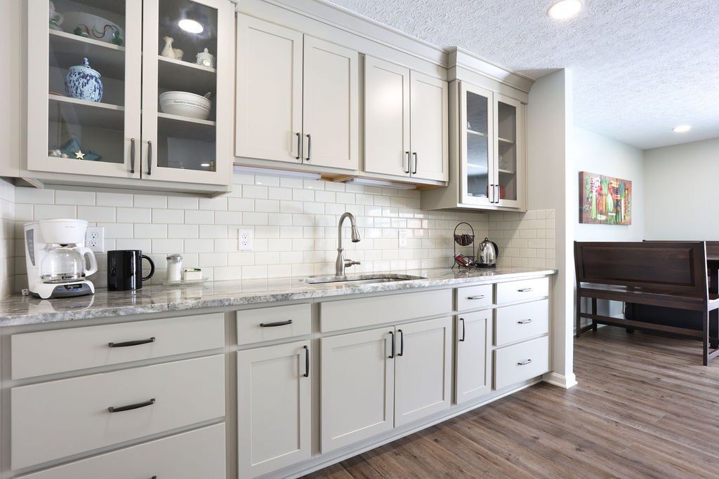 Beige kitchen cabinets with granite countertop, subway tile backsplash, and stainless steel faucet.