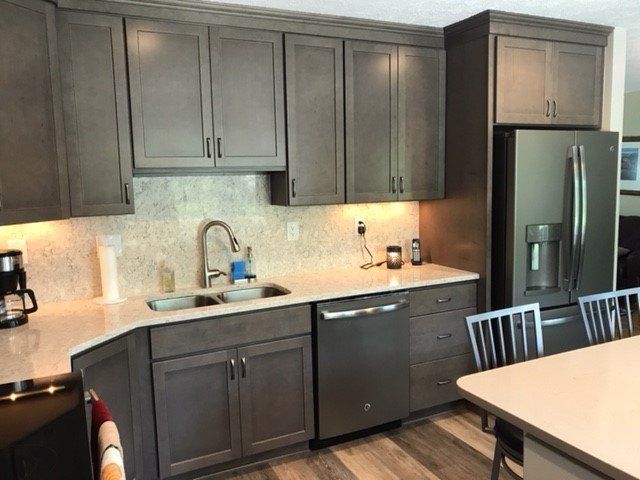 Gray kitchen cabinets with stainless steel appliances, white countertops, and a patterned backsplash.