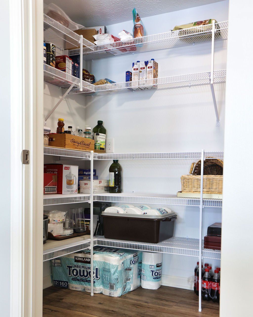 Pantry with white wire shelving holding food items, paper towels, and a storage bin.
