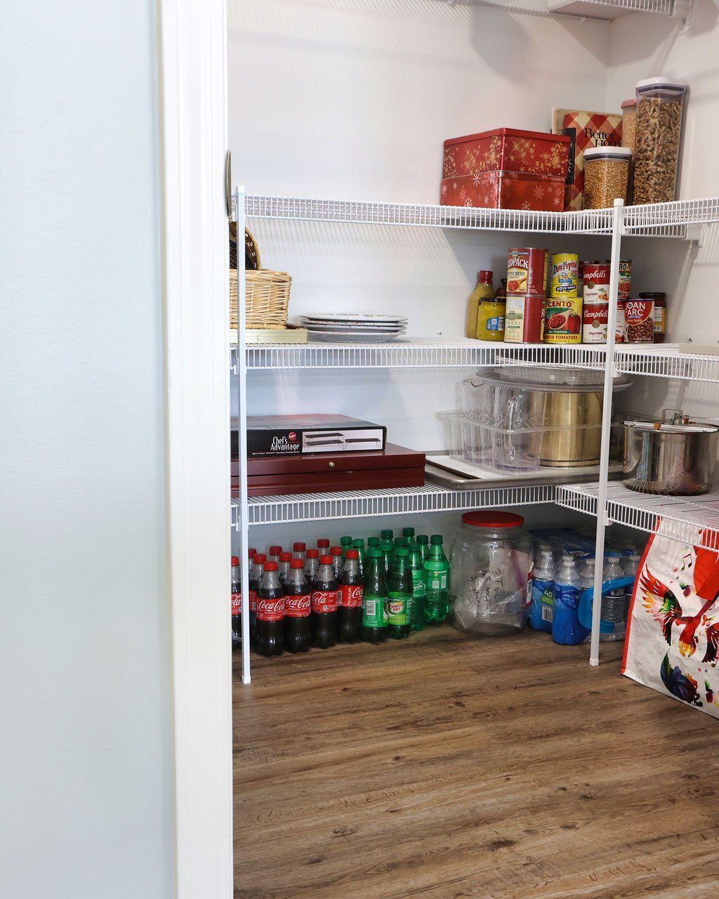A pantry with wire shelves stocked with food, beverages, and other items; wooden floors.