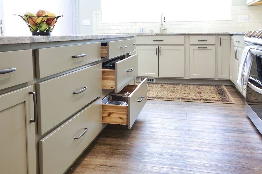 Bright kitchen with white cabinets, open drawers, and a fruit bowl on a granite countertop.