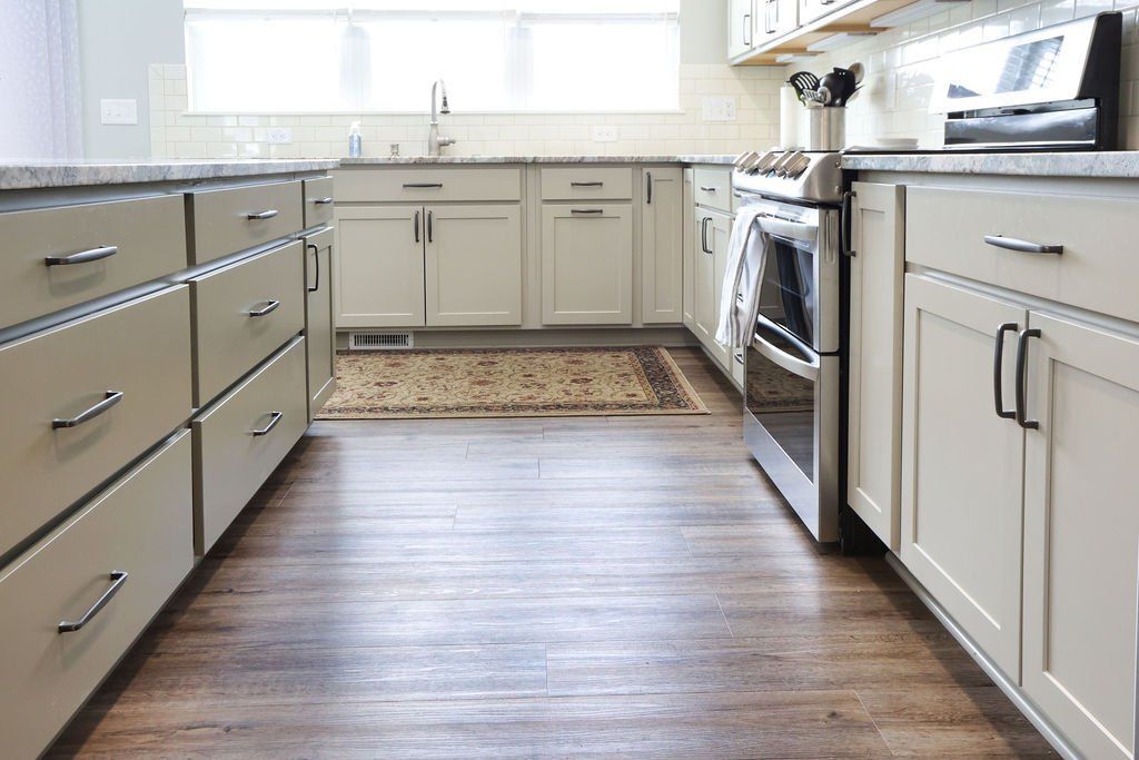 A kitchen with light-colored cabinets, granite countertops, stainless steel appliances, and dark wood flooring.