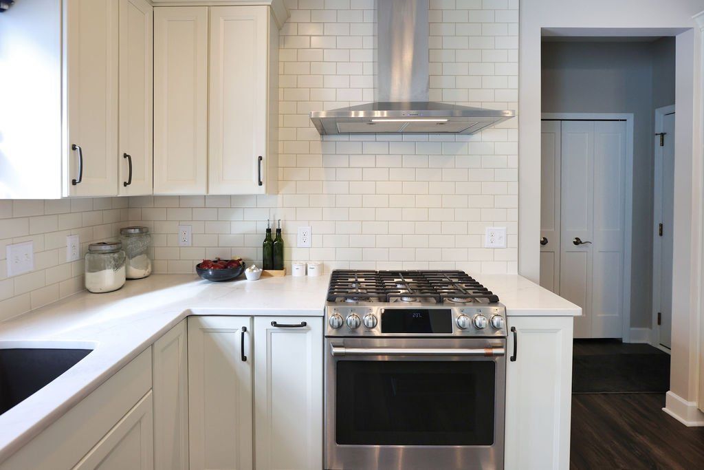 White kitchen with stainless steel range, subway tile backsplash, and dark wood flooring.