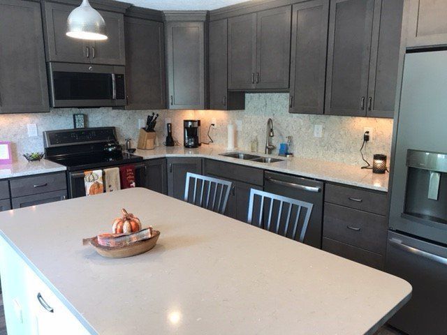 Modern kitchen with gray cabinets, white countertops, and an island; stainless steel appliances.