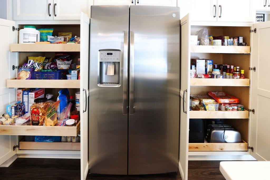Kitchen with a stainless steel refrigerator flanked by two white pantry cabinets with pull-out shelves filled with food.