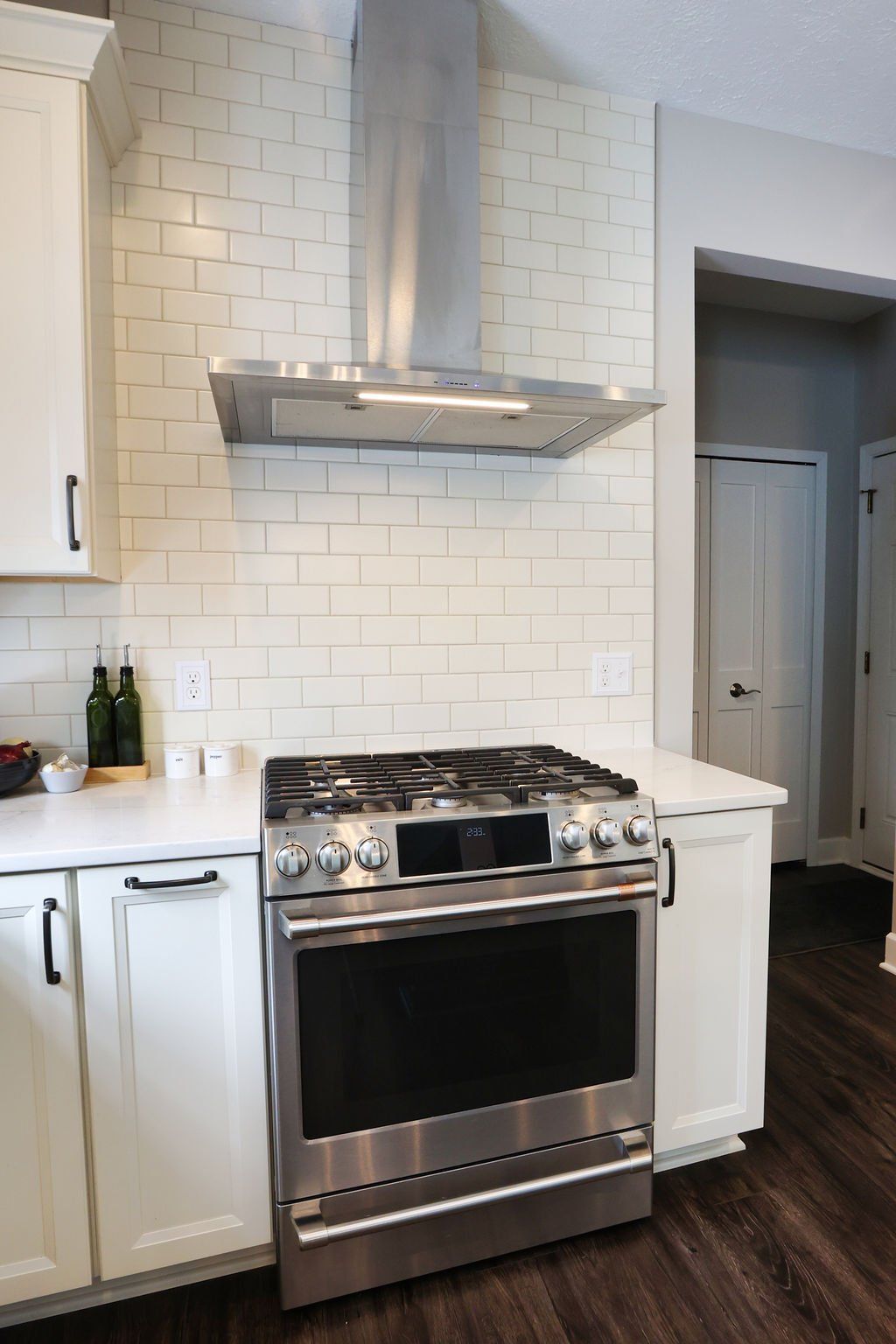 Modern kitchen with stainless steel stove and range hood, white tile backsplash, and white cabinets