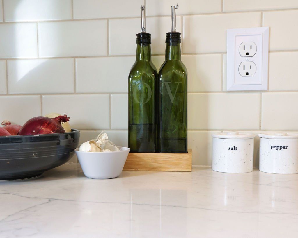 Kitchen countertop with olive oil bottles, spices, and a bowl of fruit.