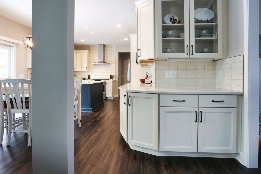 Bright kitchen with white cabinets, dark wood floors, and a doorway opening to a living area.