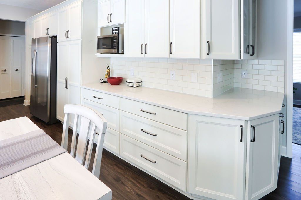 Bright white kitchen with stainless fridge, microwave, and built-in cabinetry along a long counter.