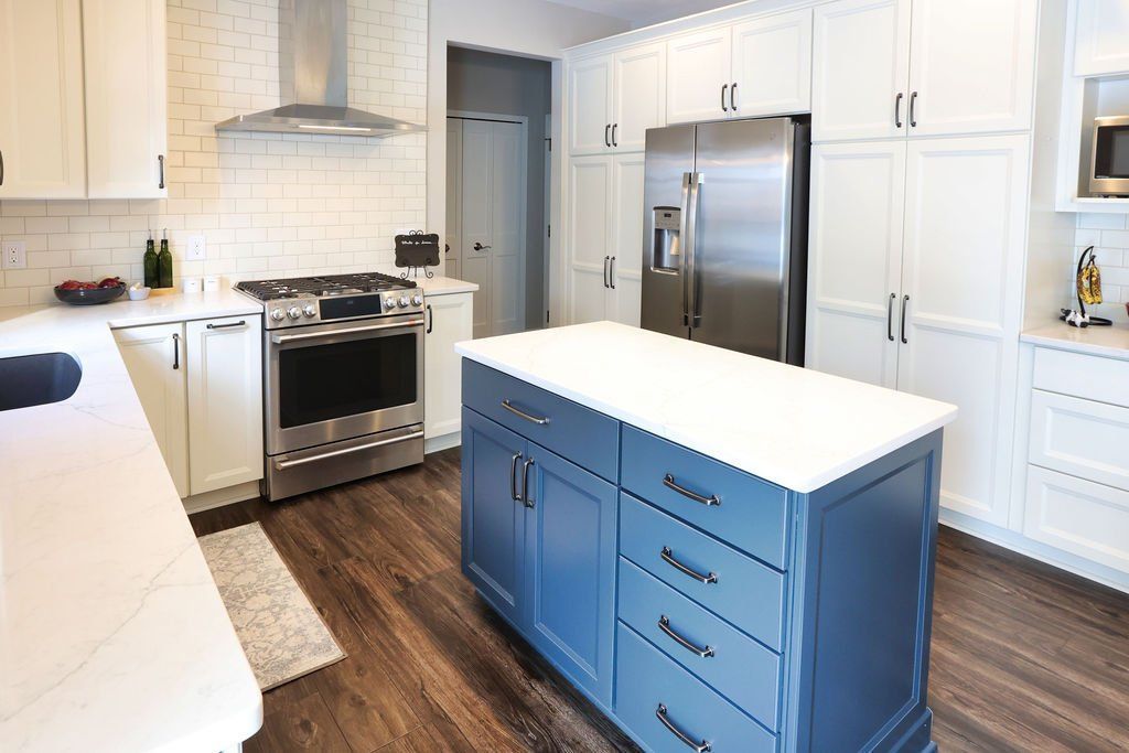 Blue kitchen island with white countertop in a modern kitchen with white and stainless steel appliances.