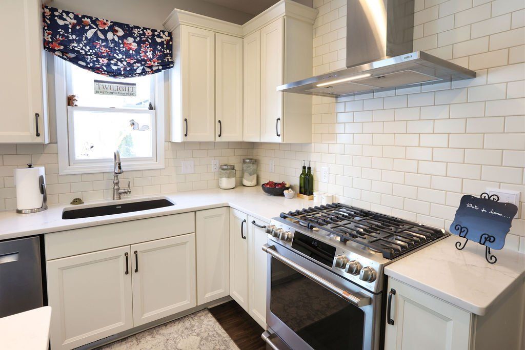 White kitchen with cabinets, stainless steel stove, and floral window treatment.