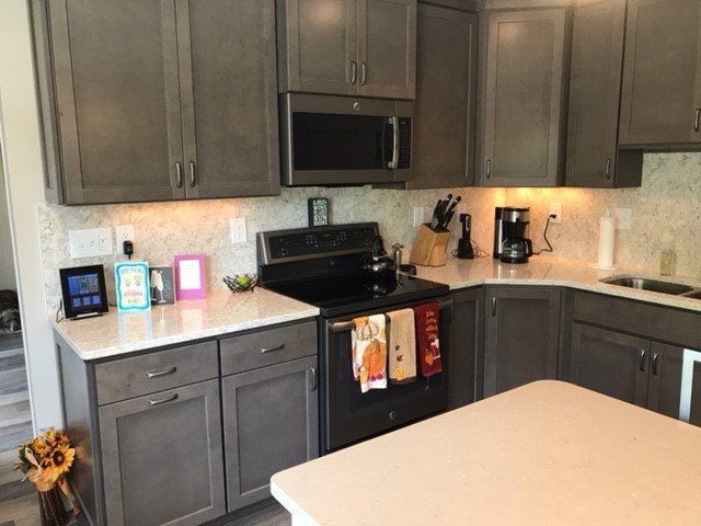 Gray kitchen with white countertops, cabinets, and island, black appliances, and patterned backsplash.