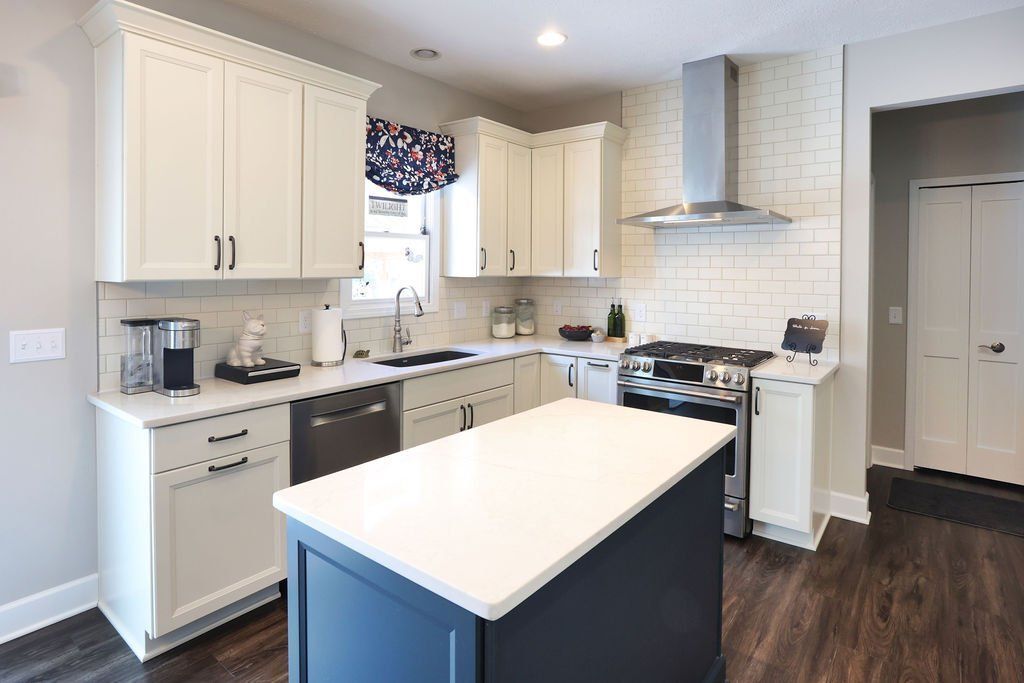 White kitchen with navy island, white cabinets, stainless steel appliances, and dark wood floors.