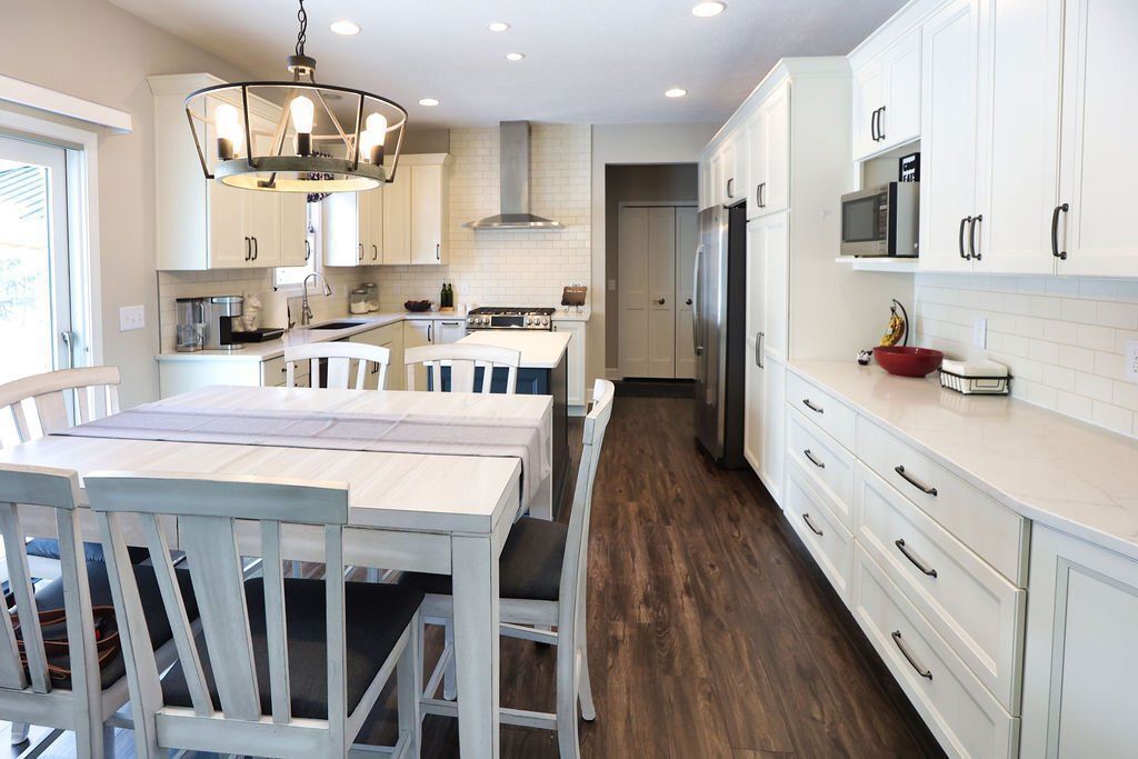 Bright white modern kitchen with island, dining table, pendant light, and dark wood floors