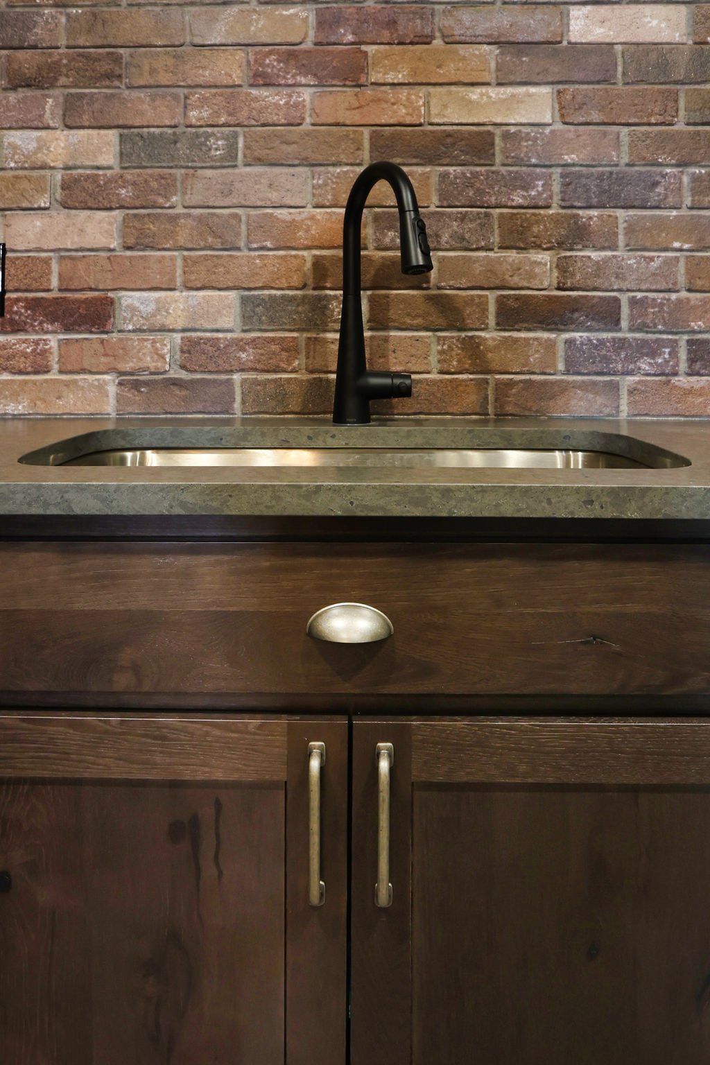 Dark brown cabinetry with a stainless steel sink, black faucet, and brick backsplash.