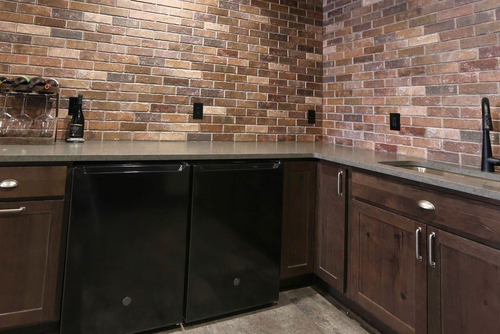 Brick-walled wet bar with black appliances, dark cabinets, and a gray countertop.
